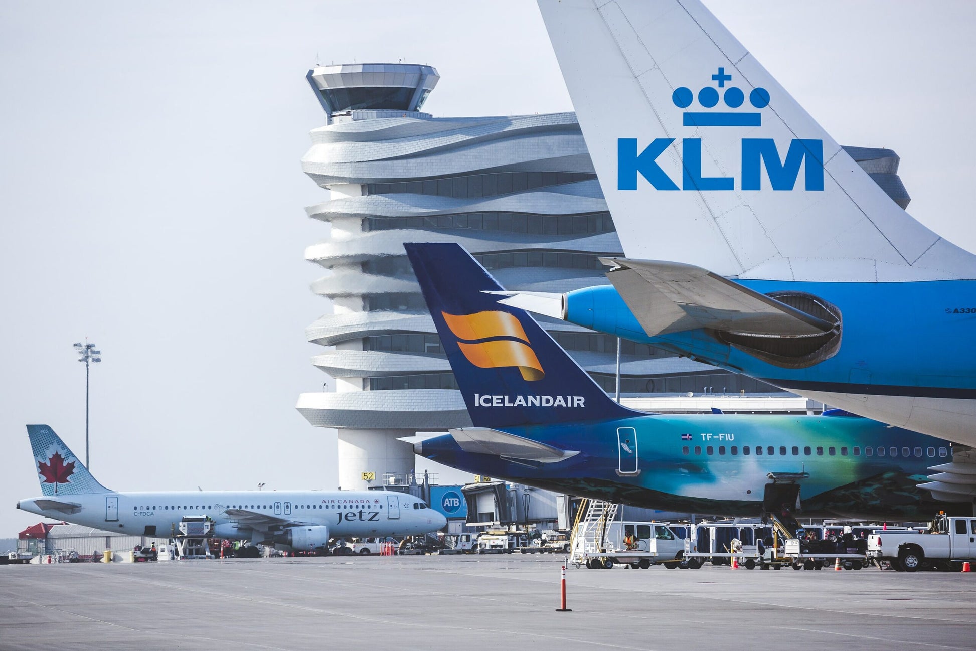 Two airplanes, one with KLM logo and another with Icelandair logo, at an airport with a control tower in the background.