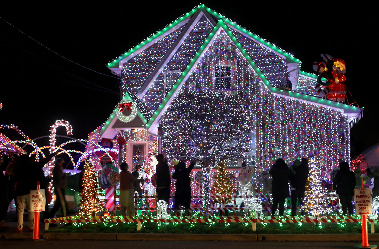 Decorative house covered in Christmas lights with people around it at night.