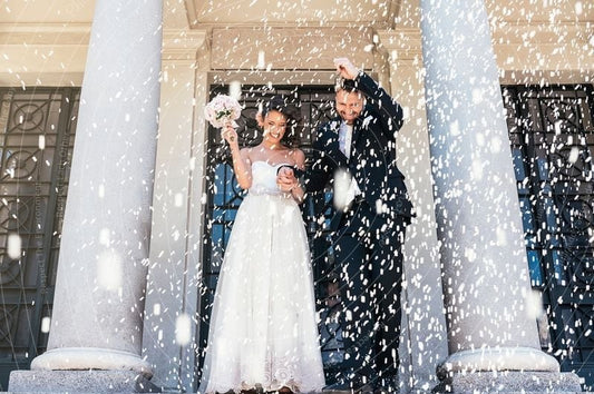Wedding couple standing in front of classical architecture with confetti falling.